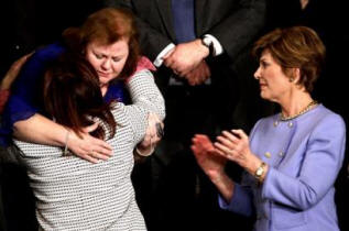 First lady Laura Bush, right, applauds as Safia Taleb al-Suhail, leader of the Iraqi Women's Political Council, back to camera, hugs Janet Norwood of Pflugerville, Texas, on Capitol Hill Wednesday, Feb. 2., 2005 during President Bush's State of the Union address. Mrs.Norwood's son Sgt. Byron Norwood was killed in Iraq last Nov.  (AP Photo/Gerald Herbert)